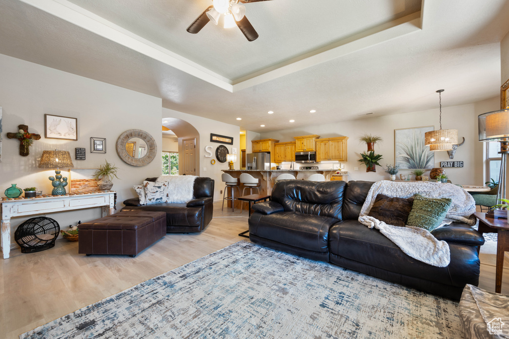 Living room with arched walkways, a ceiling fan, light wood-style floors, a raised ceiling, and recessed lighting