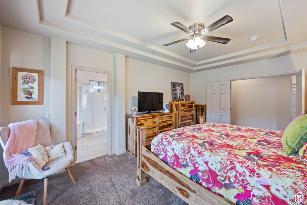 Tiled bedroom with a tray ceiling, carpet floors, ensuite bathroom, and ceiling fan