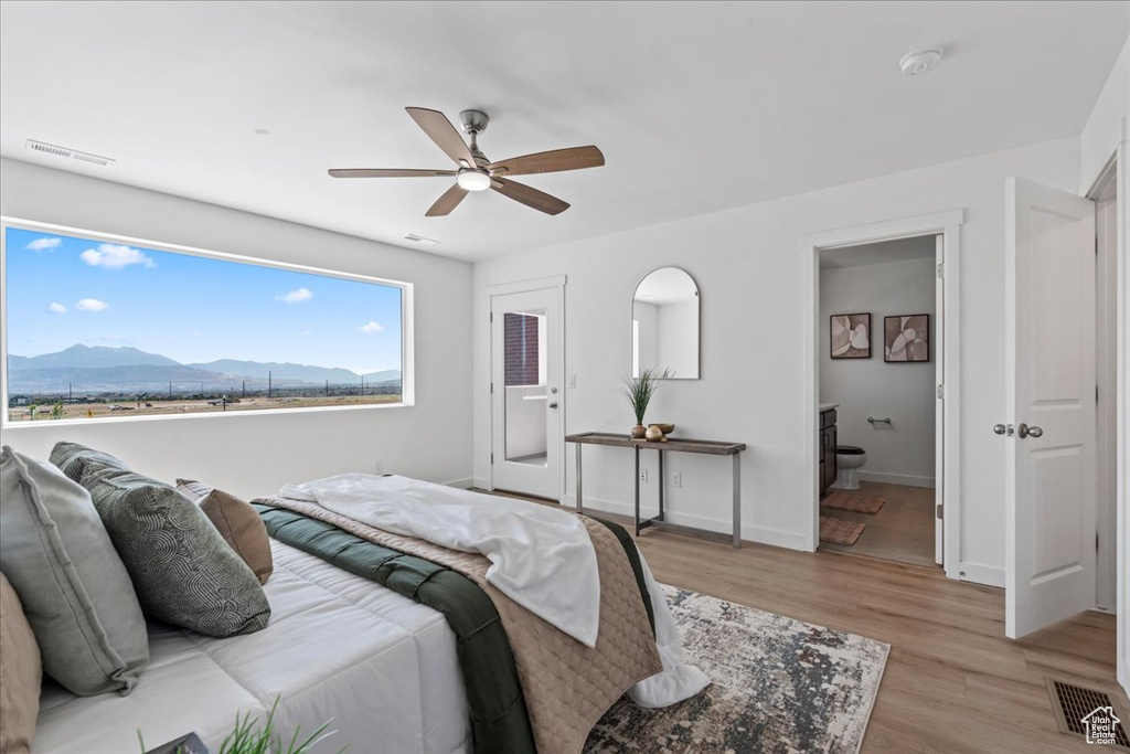 Bedroom with a mountain view, light wood-type flooring, a ceiling fan, and connected bathroom