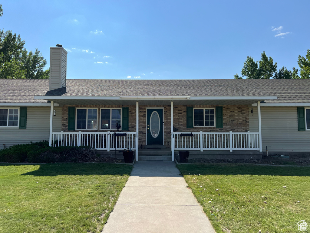 Single story home with covered porch, a front lawn, and a chimney