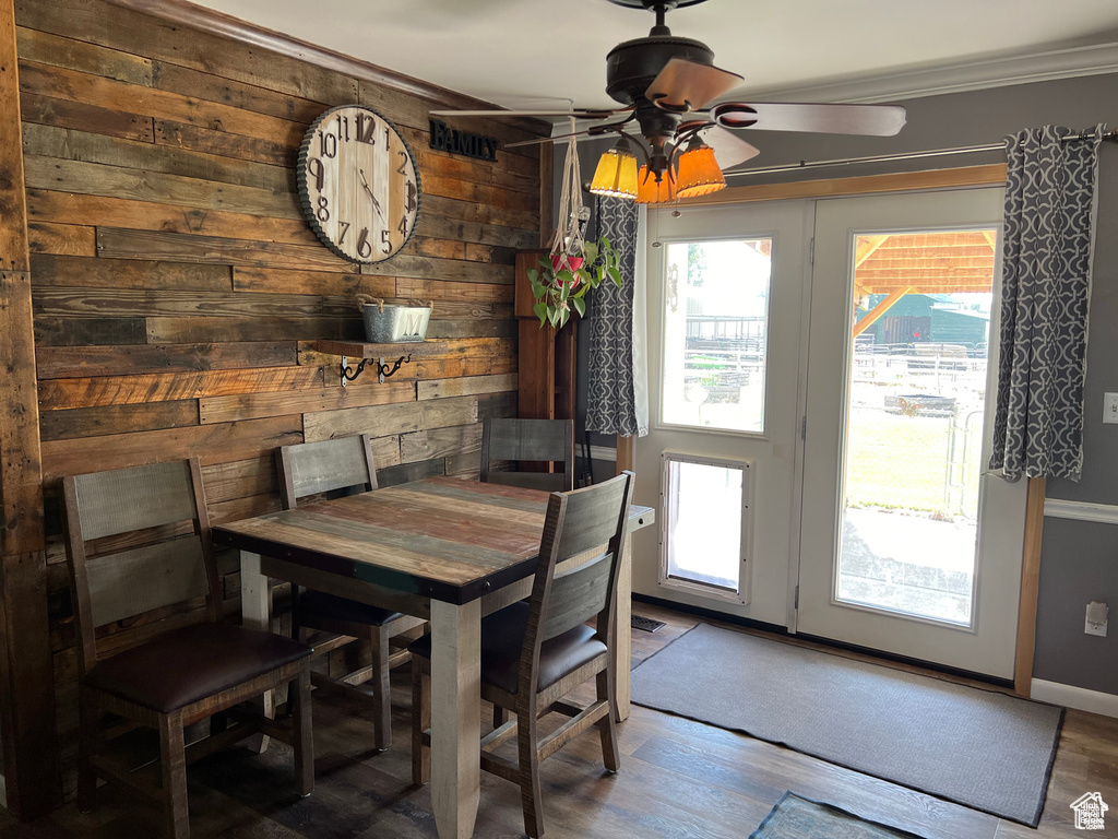 Dining area with wood walls, a ceiling fan, crown molding, and wood finished floors