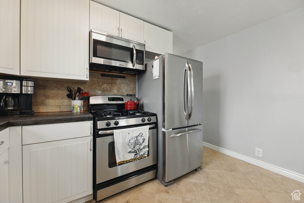 Kitchen with stainless steel appliances, tasteful backsplash, white cabinets, dark countertops, and light tile patterned flooring