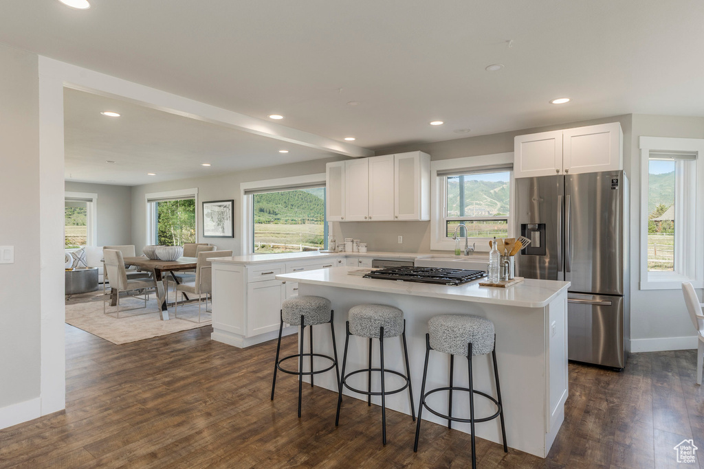 Kitchen featuring appliances with stainless steel finishes, a center island, dark wood-style flooring, a breakfast bar, and white cabinetry