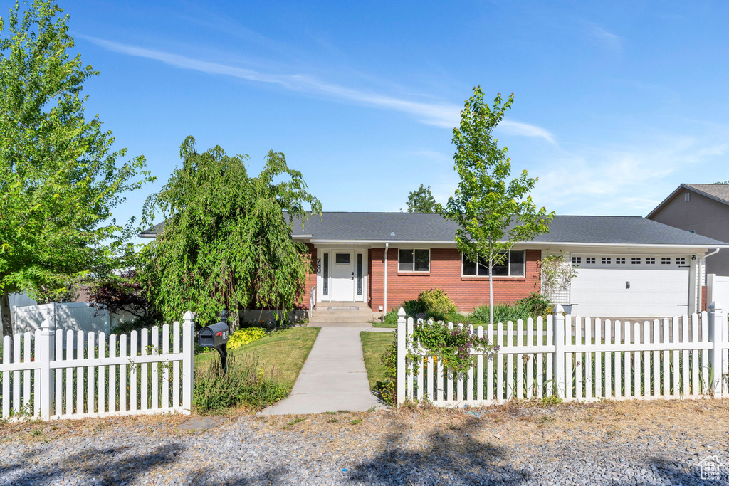 View of front facade featuring a fenced front yard, a garage, brick siding, and driveway