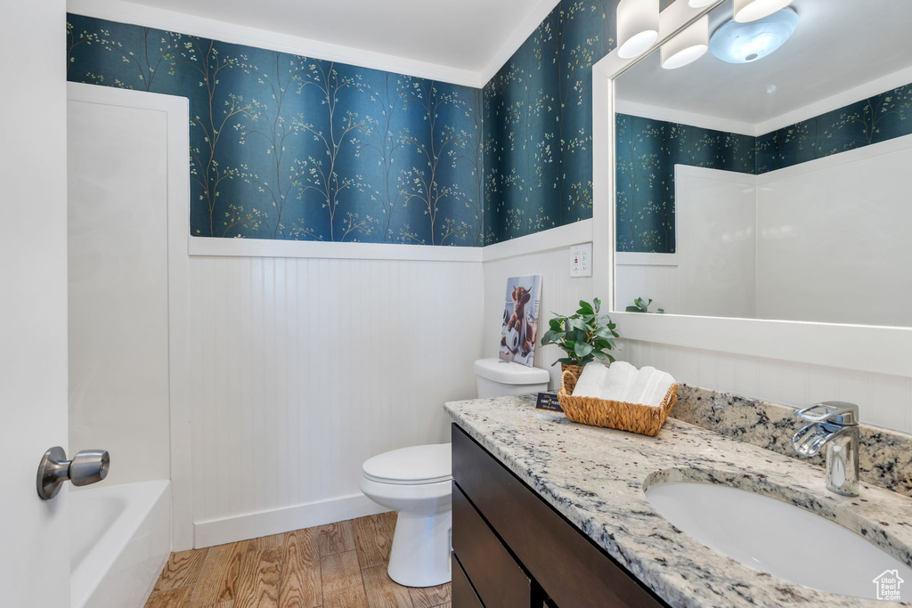 Full bath with wood finished floors, vanity, a wainscoted wall, and wallpapered walls