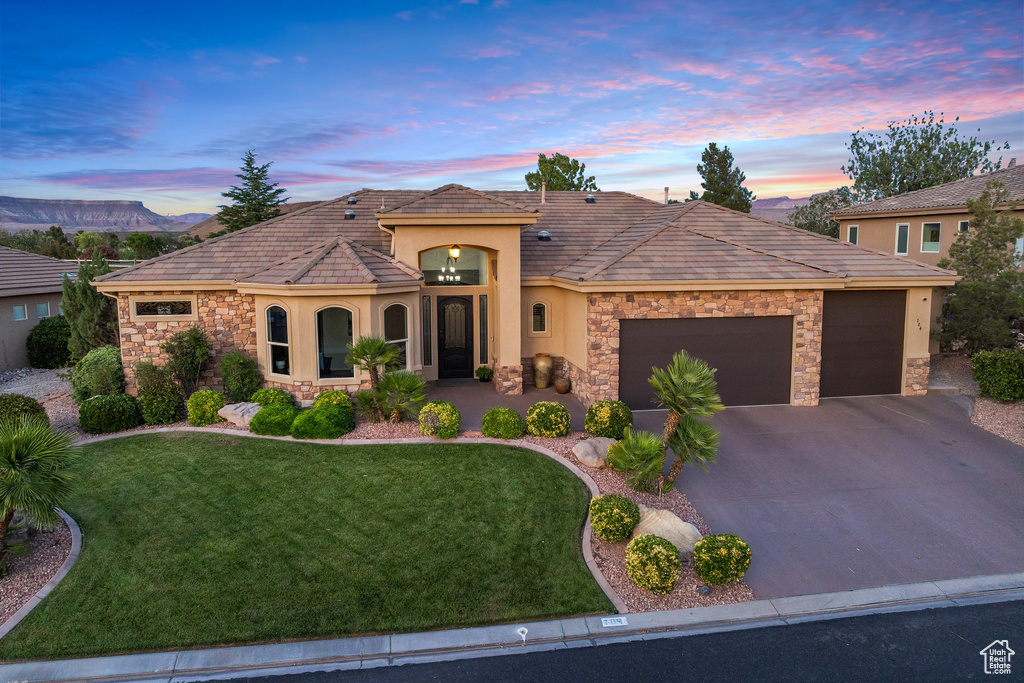View of front of home with stone siding, stucco siding, an attached garage, and a lawn
