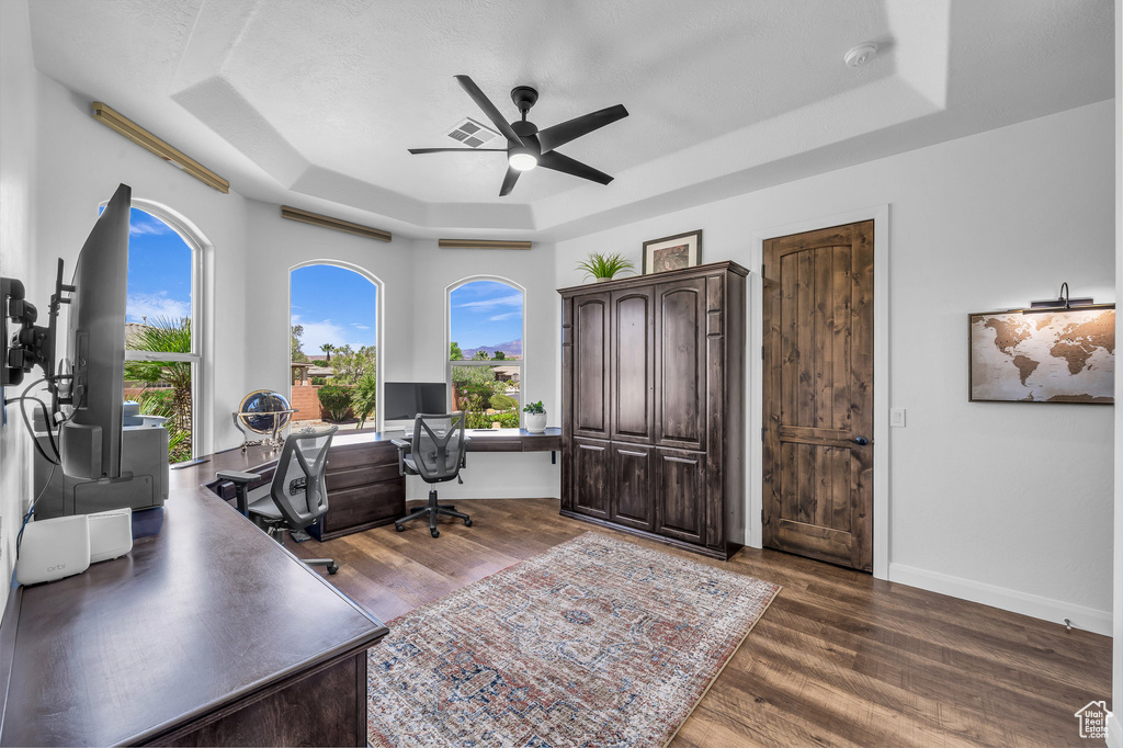 Office area with a tray ceiling, a ceiling fan, and dark wood finished floors