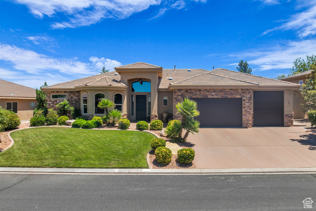 Mediterranean / spanish house with stone siding, a tile roof, an attached garage, and stucco siding