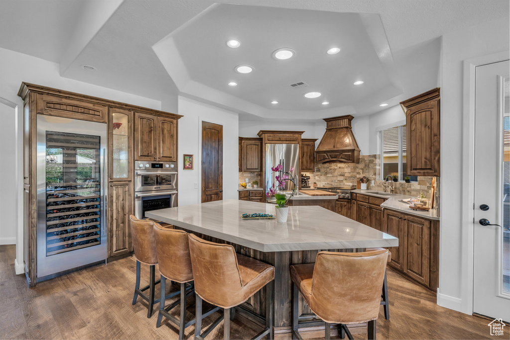 Kitchen featuring wine cooler, custom exhaust hood, stainless steel appliances, a center island, and dark wood finished floors