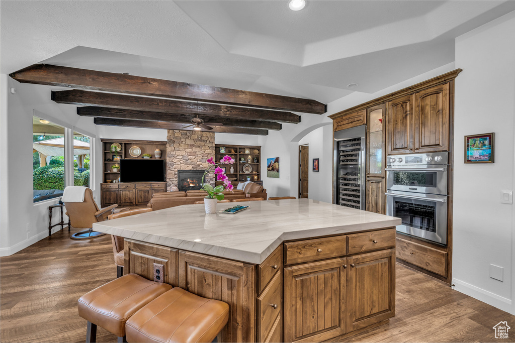 Kitchen with beverage cooler, stainless steel double oven, arched walkways, wood finished floors, and a fireplace