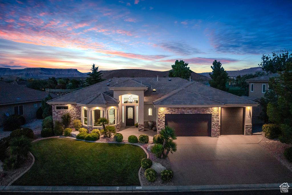 View of front facade with stone siding, an attached garage, concrete driveway, a front yard, and a mountain view