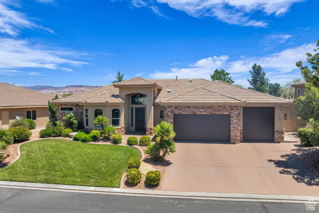 View of front of property with an attached garage, a tiled roof, stucco siding, and stone siding