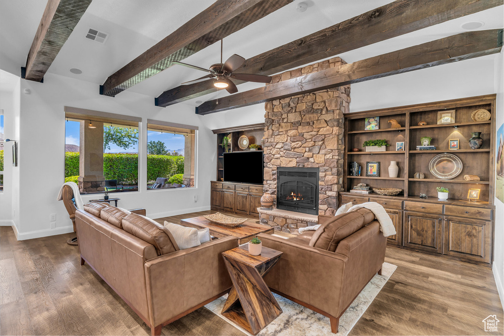 Living room featuring wood finished floors, beamed ceiling, ceiling fan, and a fireplace