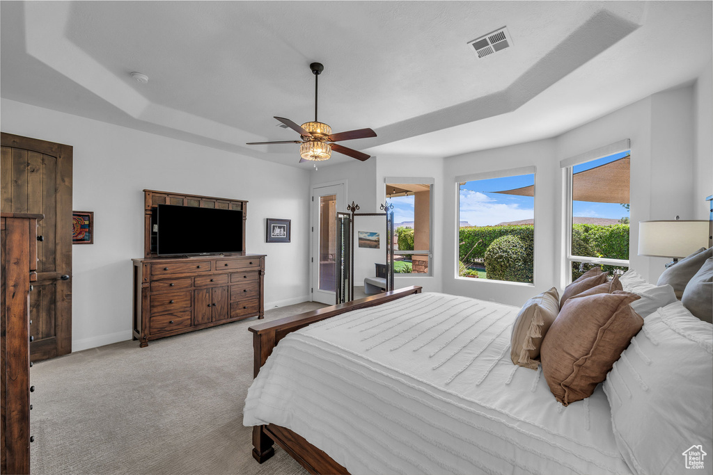 Carpeted bedroom featuring a tray ceiling, multiple windows, and a ceiling fan