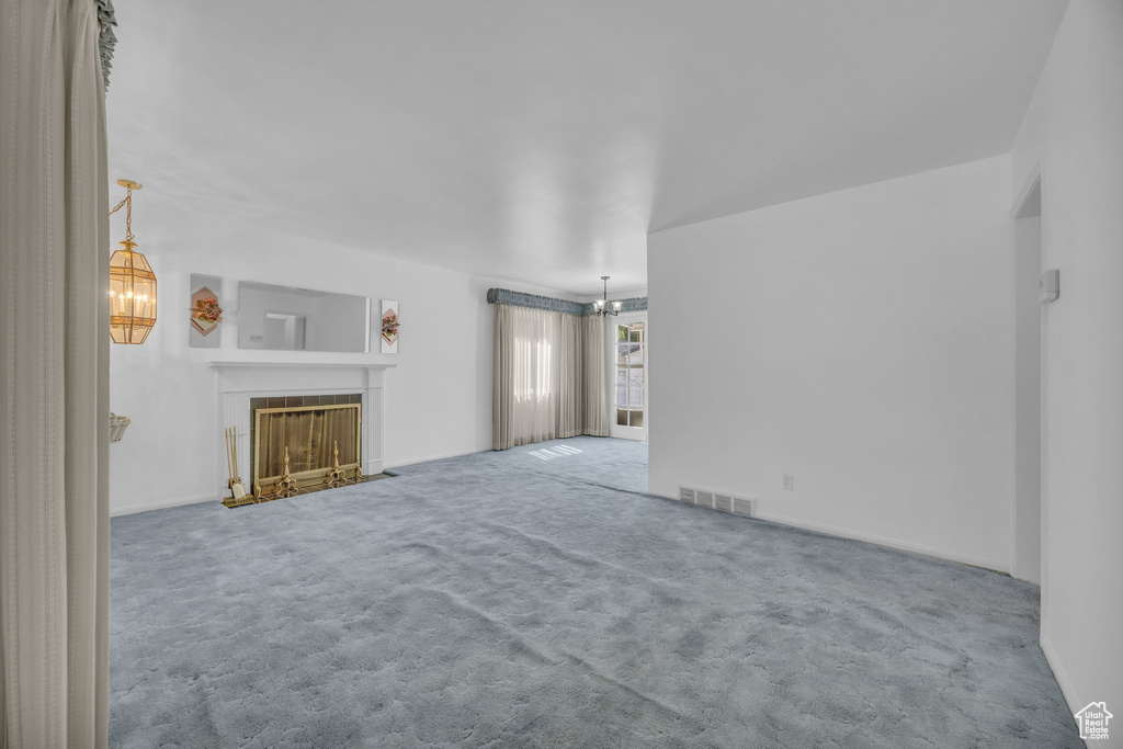 Unfurnished living room featuring a chandelier, carpet, and a fireplace