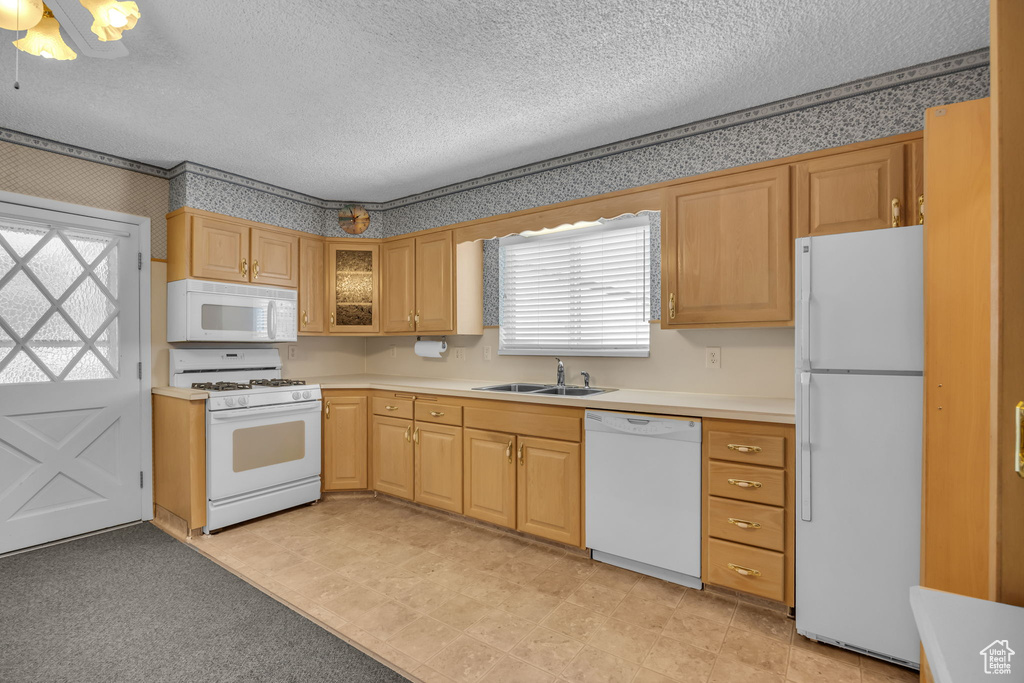 Kitchen featuring white appliances, a textured ceiling, light countertops, wallpapered walls, and glass insert cabinets