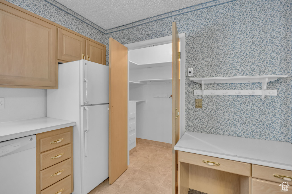 Kitchen featuring white appliances, light brown cabinetry, light countertops, and a textured ceiling