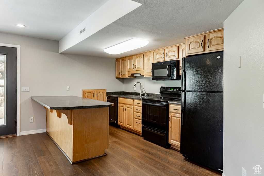 Kitchen with black appliances, a peninsula, light brown cabinets, dark countertops, and dark wood-style floors