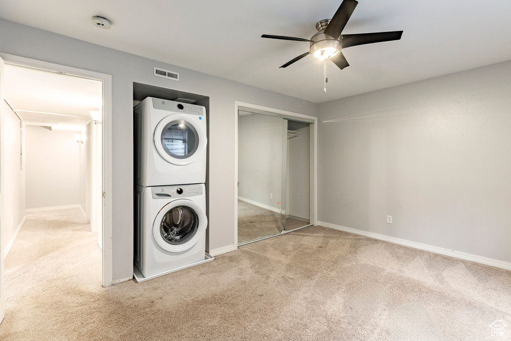 Laundry area with stacked washer and clothes dryer, carpet floors, and ceiling fan