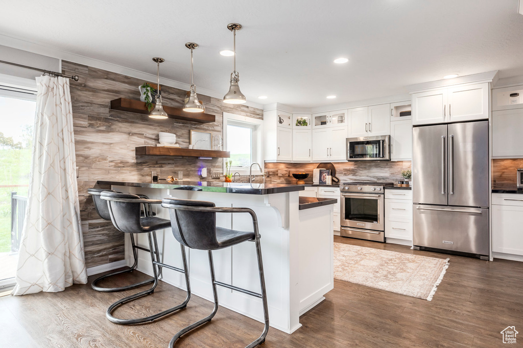 Kitchen featuring stainless steel appliances, dark countertops, a breakfast bar, backsplash, and dark wood-type flooring