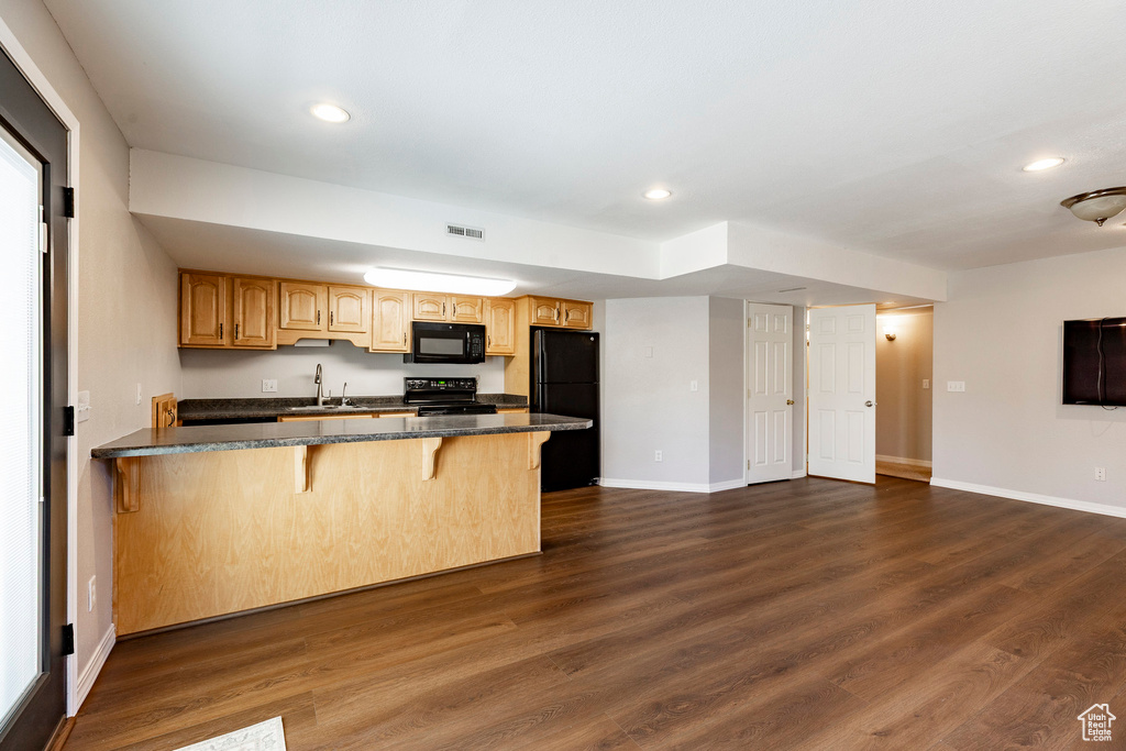 Kitchen with black appliances, a kitchen bar, a peninsula, recessed lighting, and dark wood finished floors