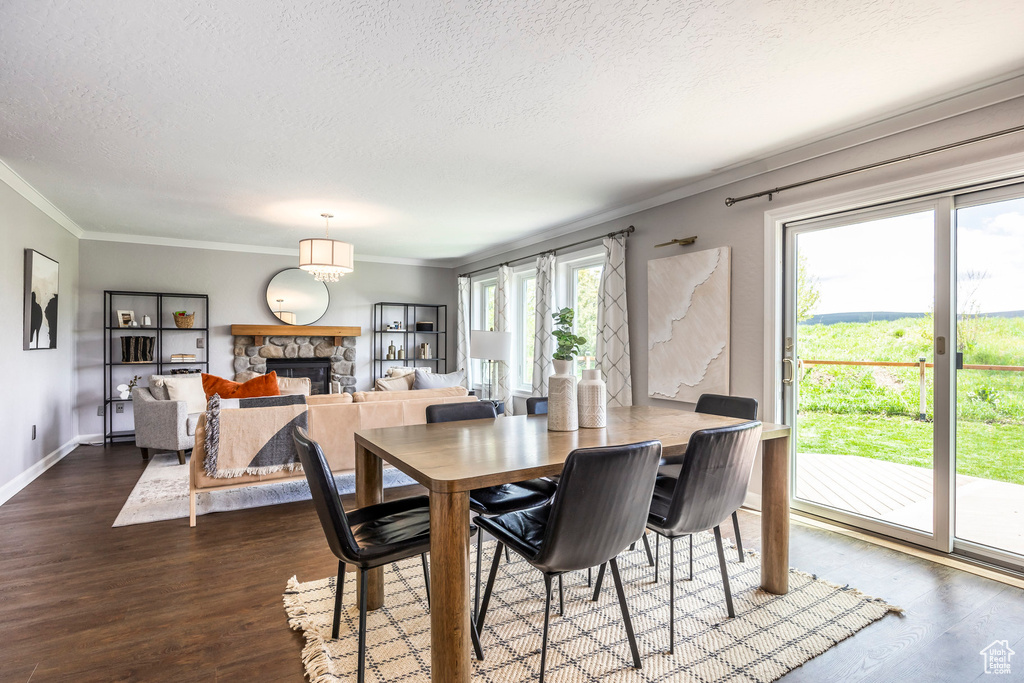 Dining room with a textured ceiling, a stone fireplace, ornamental molding, and wood finished floors