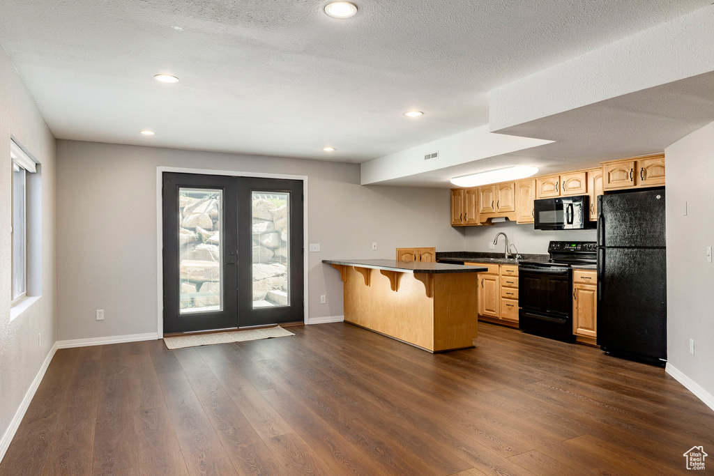 Kitchen with black appliances, a kitchen breakfast bar, a peninsula, dark wood-type flooring, and recessed lighting