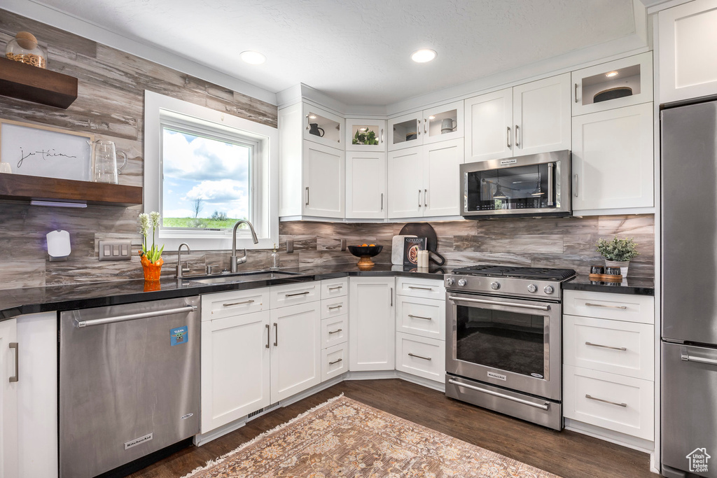 Kitchen featuring appliances with stainless steel finishes, dark wood-style floors, white cabinets, backsplash, and recessed lighting