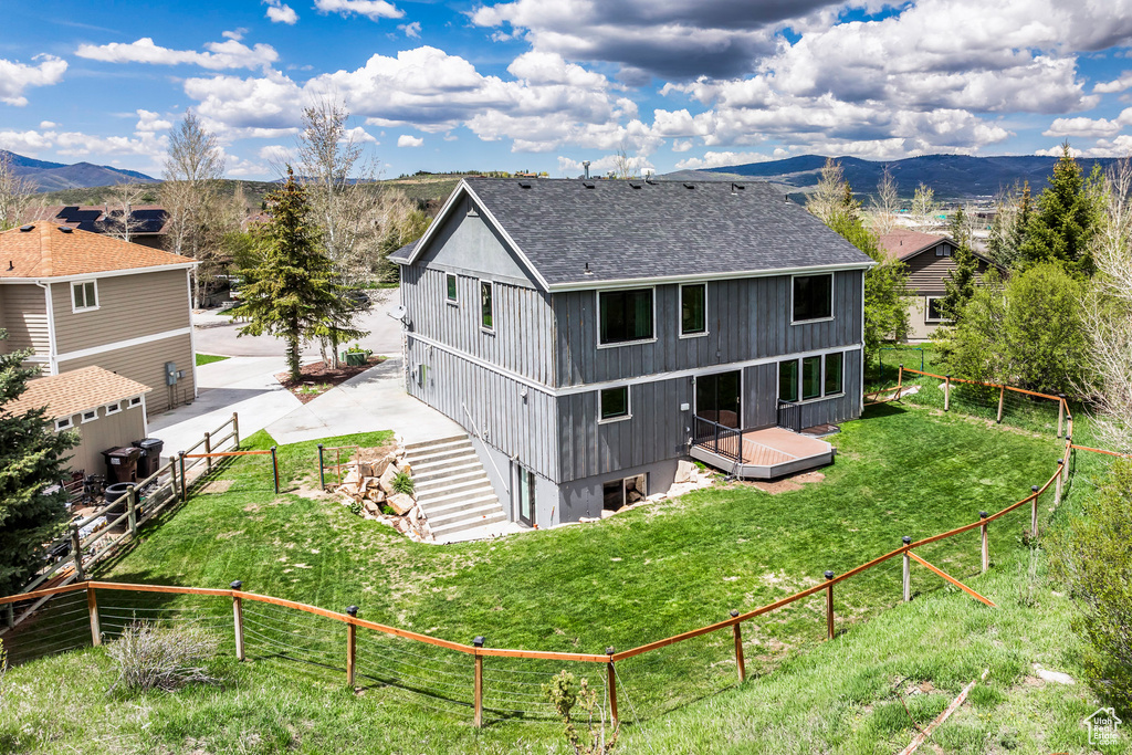 Rear view of house featuring roof with shingles, a deck with mountain view, and a fenced backyard
