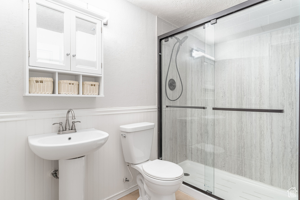 Bathroom with a shower stall, a wainscoted wall, and a textured ceiling