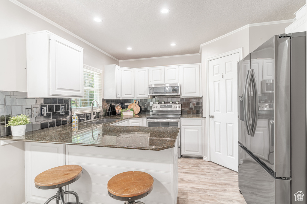 Kitchen with stainless steel appliances, a peninsula, dark stone countertops, light wood-style floors, and white cabinets
