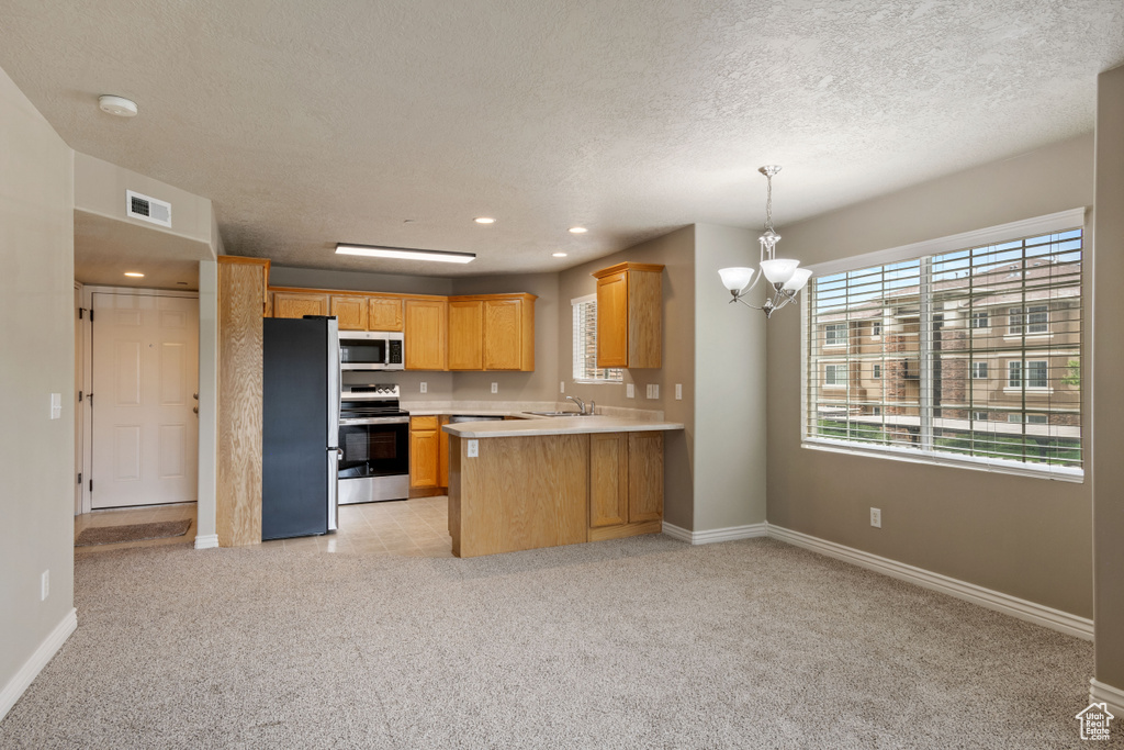 Kitchen with appliances with stainless steel finishes, a chandelier, open floor plan, light countertops, and light carpet