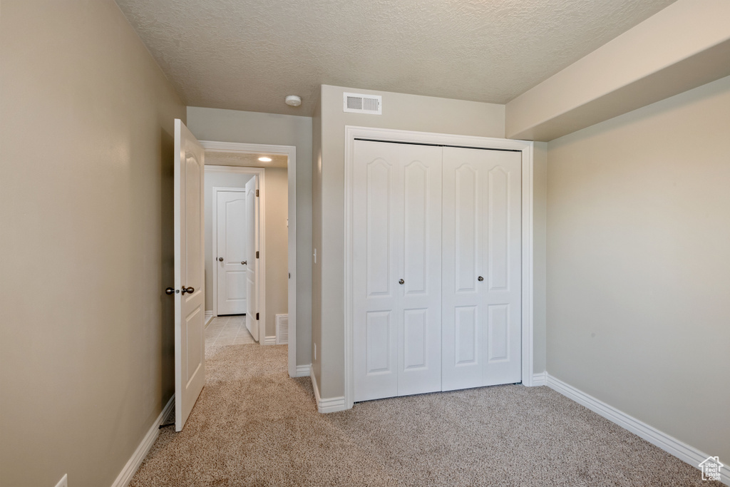 Unfurnished bedroom with light colored carpet, a textured ceiling, and a closet