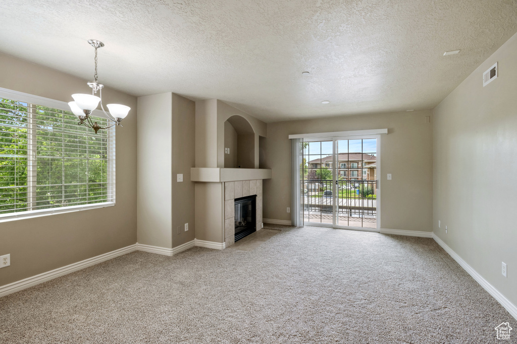 Unfurnished living room with a textured ceiling, a chandelier, light colored carpet, and a fireplace
