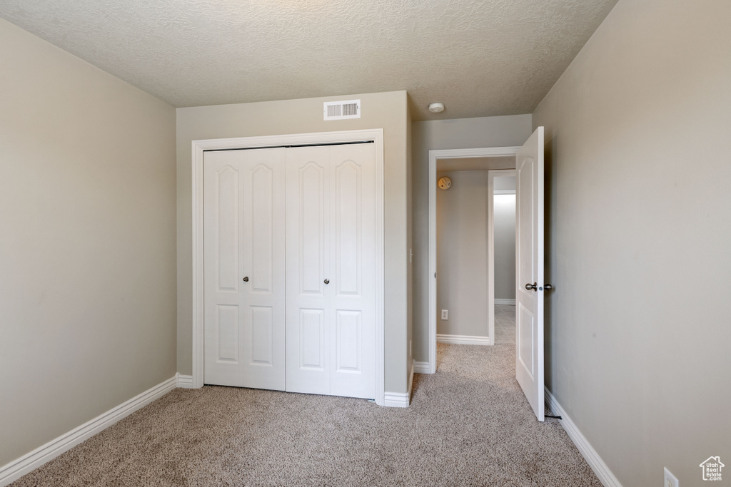 Unfurnished bedroom featuring carpet flooring, a textured ceiling, and a closet