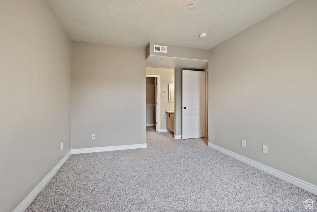 Unfurnished bedroom featuring light carpet, a walk in closet, and a textured ceiling