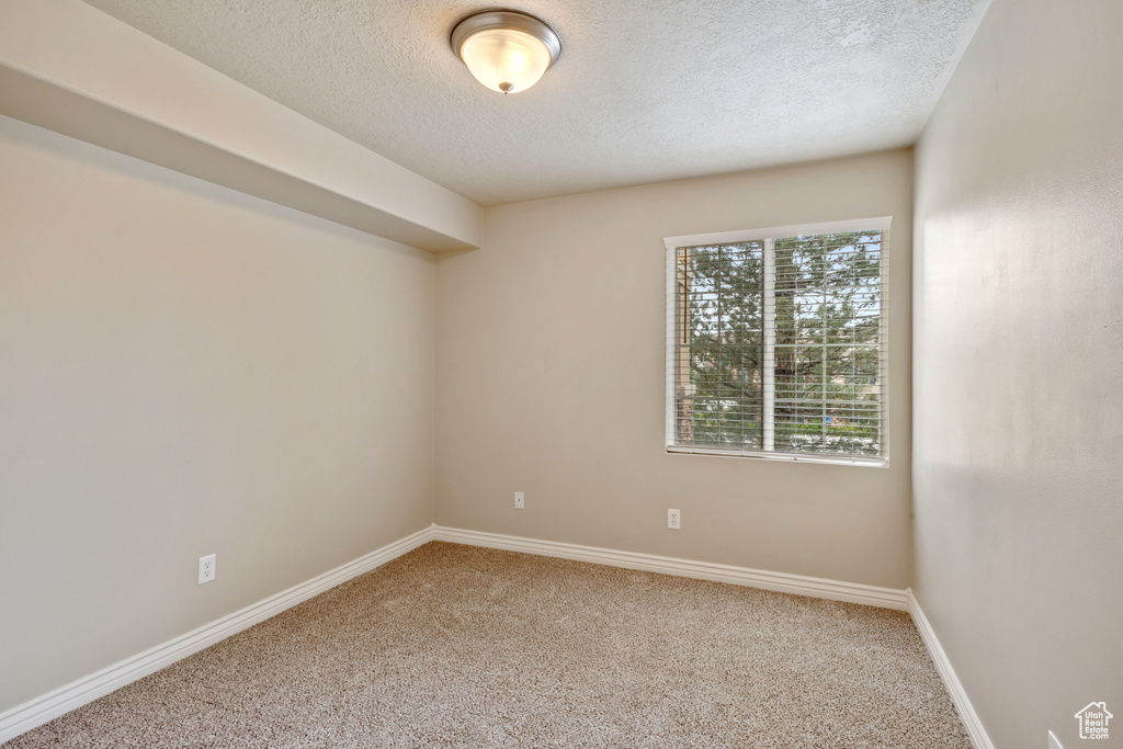 Carpeted empty room featuring a textured ceiling and baseboards