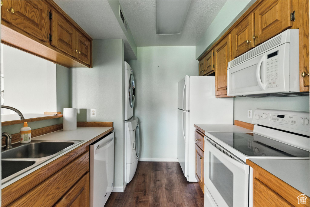 Kitchen featuring white appliances, stacked washing machine and dryer, dark wood-style flooring, brown cabinets, and light countertops