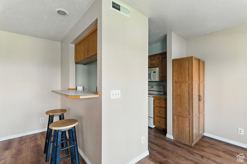 Kitchen featuring white appliances, a breakfast bar, dark wood finished floors, light countertops, and a textured ceiling