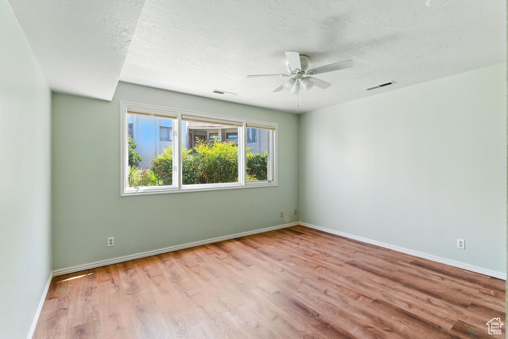 Spare room featuring wood finished floors, a ceiling fan, and a textured ceiling