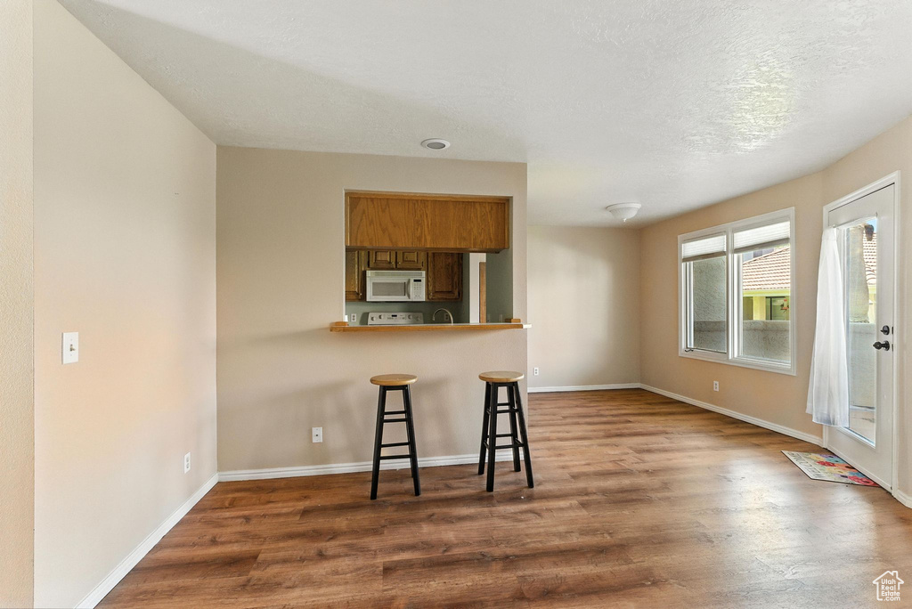 Kitchen featuring white microwave, a breakfast bar, brown cabinets, and wood finished floors