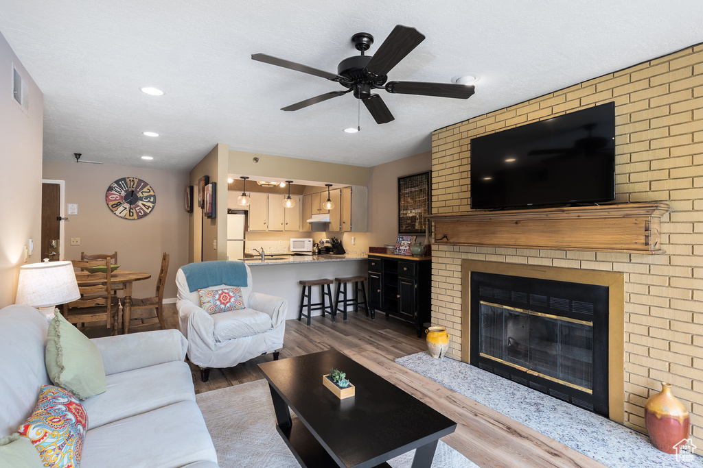 Living room featuring wood finished floors, ceiling fan, recessed lighting, and a brick fireplace