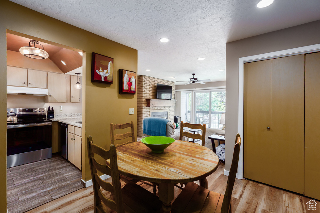 Dining area with a fireplace, ceiling fan, recessed lighting, light wood-style flooring, and a textured ceiling