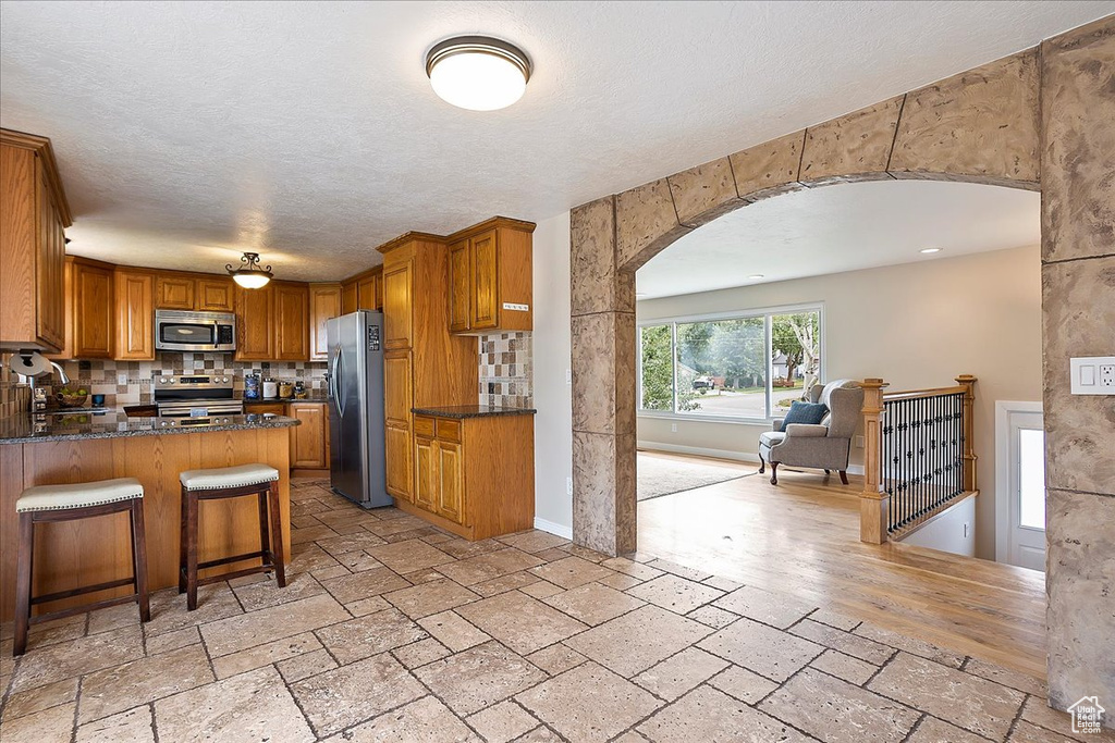 Kitchen with stainless steel appliances, arched walkways, stone tile flooring, brown cabinets, and a textured ceiling