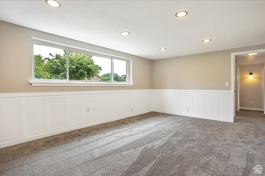 Carpeted empty room featuring a wainscoted wall, recessed lighting, and a decorative wall