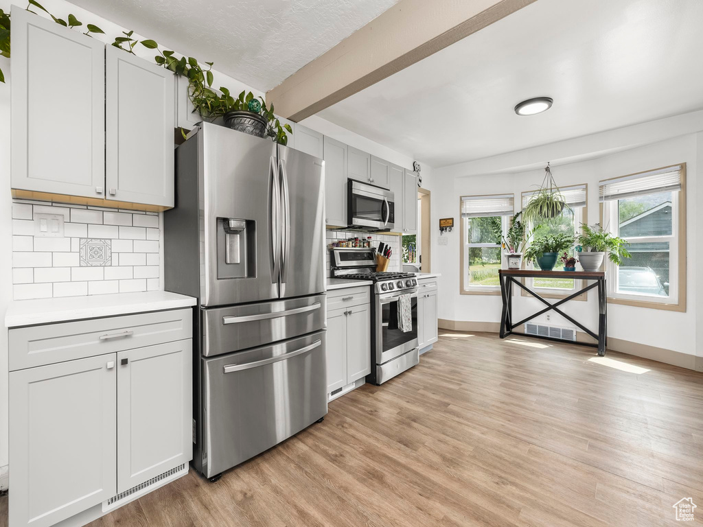 Kitchen with stainless steel appliances, light countertops, tasteful backsplash, light wood finished floors, and beam ceiling