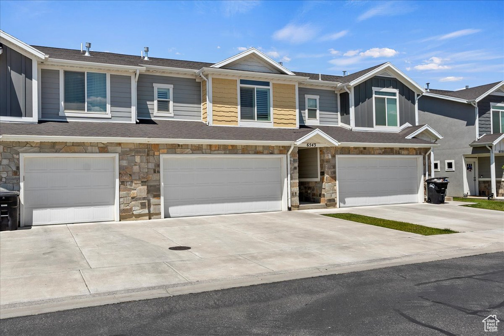 Multi unit property featuring a garage, stone siding, driveway, and board and batten siding