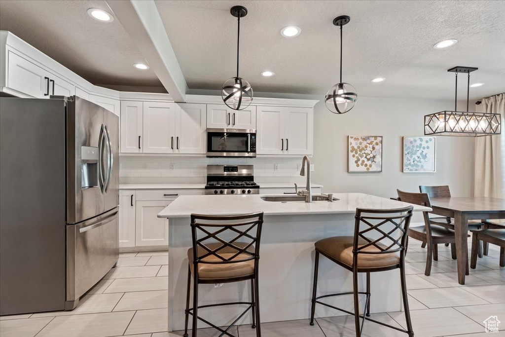 Kitchen with appliances with stainless steel finishes, light countertops, a breakfast bar, white cabinetry, and pendant lighting