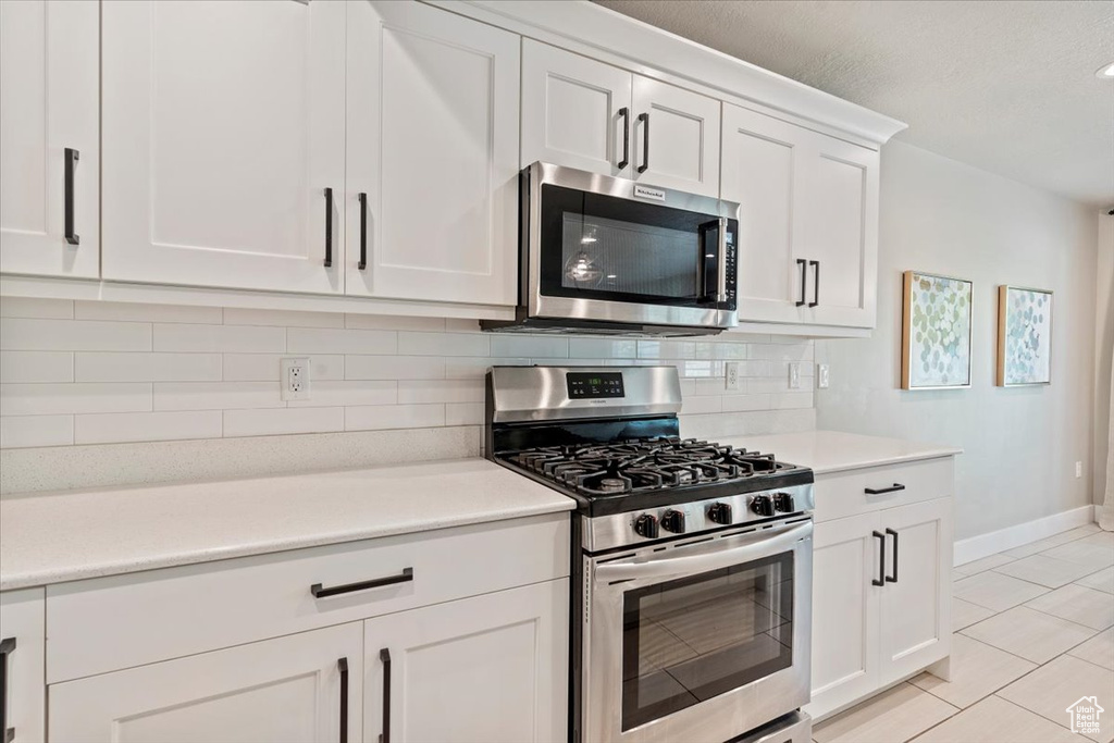 Kitchen with stainless steel appliances, decorative backsplash, light tile patterned flooring, white cabinets, and light countertops