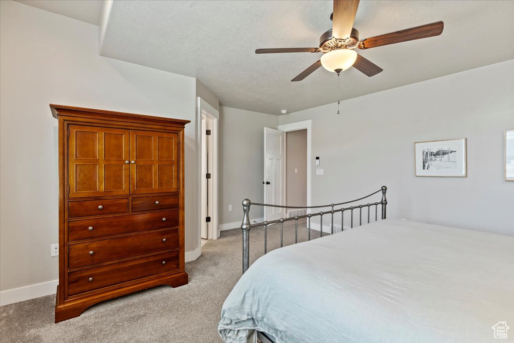 Bedroom with light colored carpet, ceiling fan, and a textured ceiling